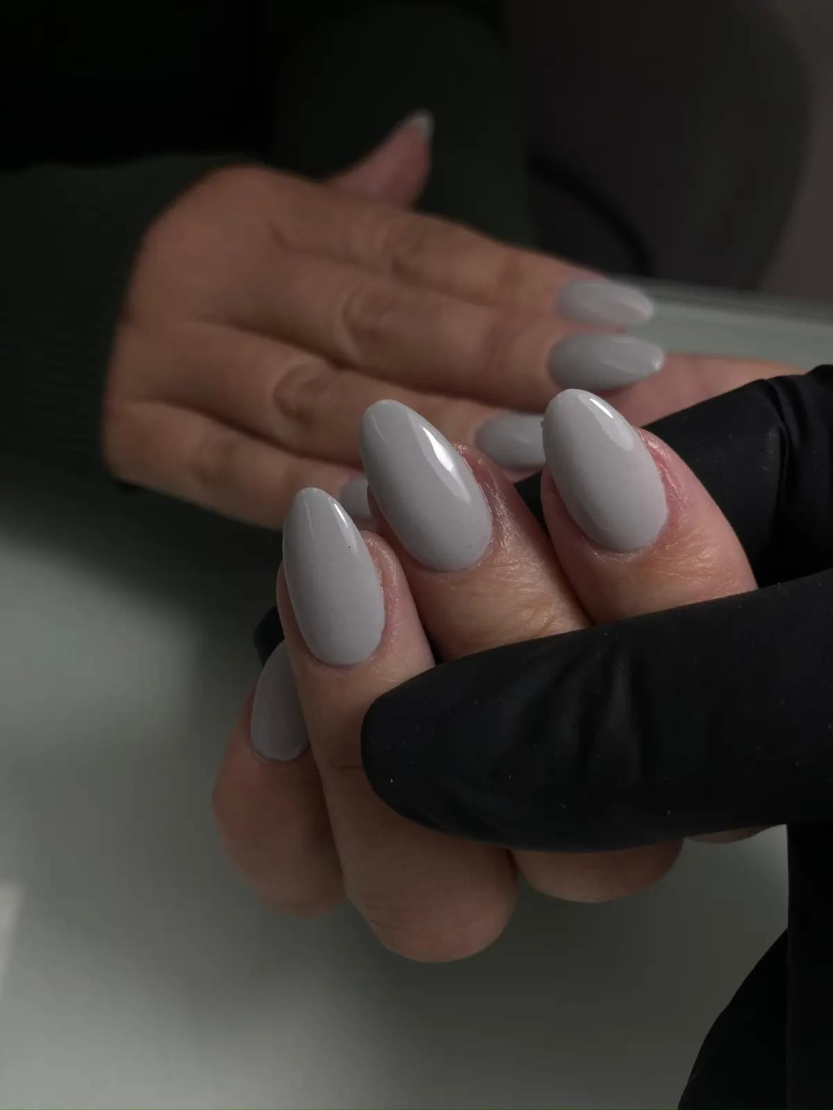 Almond nails in pearl grey gel, held by the technician